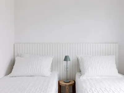 A minimalist bedroom with two beds, white bedding, and a small wooden table with a lamp.