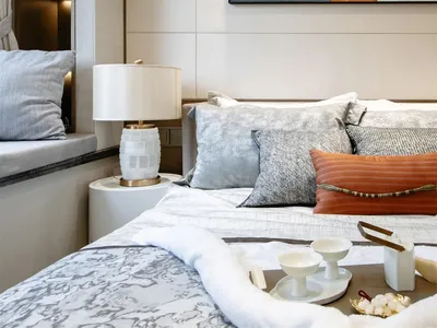 A minimalist bedroom featuring a bed with marble and fabric textures, complemented by a marble lamp and a wall-mounted abstra