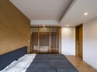 A minimalist bedroom with bamboo laminate flooring and a textured wall.