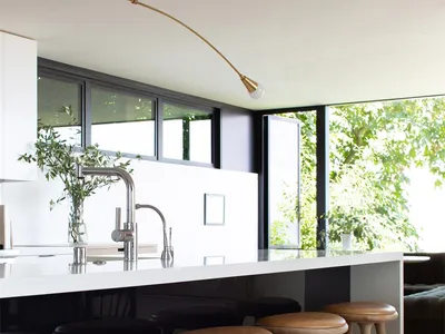 A modern kitchen featuring wooden stools and a white countertop with a sink and faucet.