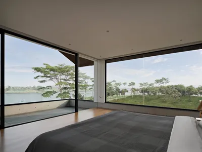 Modern bedroom with glass walls overlooking a serene lake with a grassy landscape.