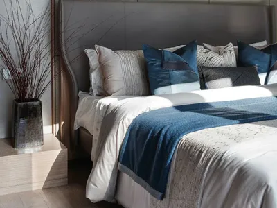 A modern minimalist bedroom featuring a custom upholstered headboard adorned with patterned throw pillows, white bedding, and