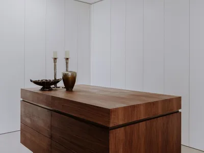 A modern, minimalist bedroom featuring an elegant wooden dresser and white walls.