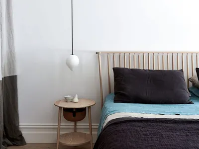 Bedroom with minimalist design featuring a wooden headboard, woolen blanket, and linen bedding on a wooden floor with a hangi