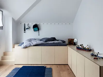A minimalist bedroom with a wooden bed platform and a blue rug on a wooden floor.