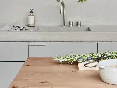 Modern minimalist residential kitchen with concrete countertop and fixtures, featuring greenery and sleek design.
