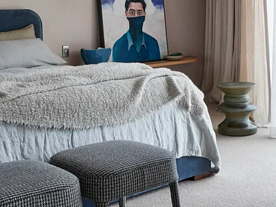 A modern bedroom featuring a bed with gray bedding, a dark blue bed frame, and a hanging sconce above it, alongside a portrai