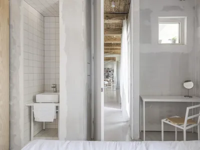 Modern minimalist bedroom with concrete walls, wood accents, and white furniture.