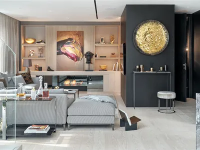 A modern minimalist living room with a gray sectional sofa, a glass coffee table, and a sleek fireplace with a golden decorat