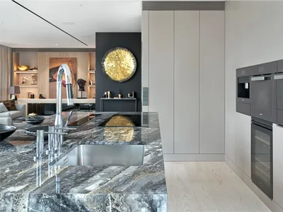 Modern kitchen featuring a marble countertop with stainless steel appliances and a circular golden light fixture.