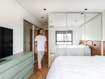 A modern minimalist bedroom with large floor-to-ceiling mirrors, white bed linens, and wooden flooring.
