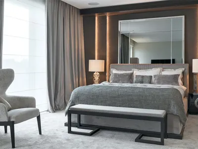 A modern minimalist bedroom featuring a grey upholstered bed, a bench, and two台 lamps, all set against a wall of mirrors and