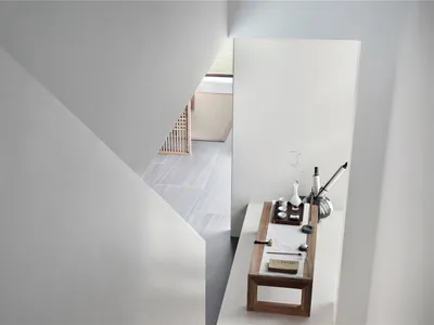 A minimalist bedroom featuring concrete walls and floors with a small table holding a vase and writing implements.