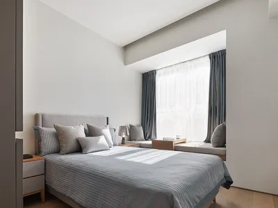 A minimalist bedroom with a bed covered in grey and white striped bedding, grey pillows, and curtains on a window