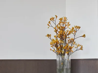 A modern home office desk with a vase of flowers, a book, and a comfortable upholstered chair.