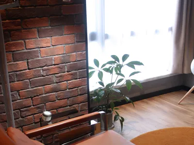 A cozy industrial-style living room features a modern leather chair, metallic frame, wooden floor, and brick accent wall.