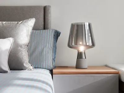 A modern bedroom featuring a wooden headboard, concrete bedside table, and glass lamp.