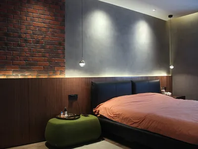 A minimalist bedroom featuring a brick wall, a black bed frame, and a green ottoman.