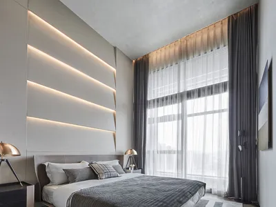 A minimalist bedroom with a gray floating bed, illuminated wall panel, and large windows with dark curtains.