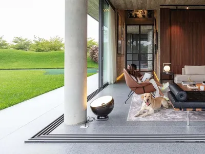 A modern industrial living room with concrete walls and floor, featuring a woman relaxing in a chair and a dog lying on the f