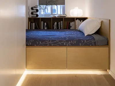 A minimalist bedroom featuring a wooden frame bench with a blue floral bedspread and a white pillow.