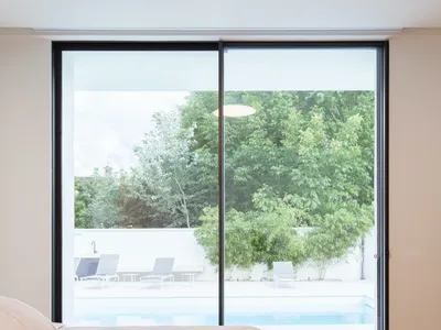 Modern minimalist bedroom with a large glass window overlooking a pool and garden, featuring wooden flooring and a comfortabl