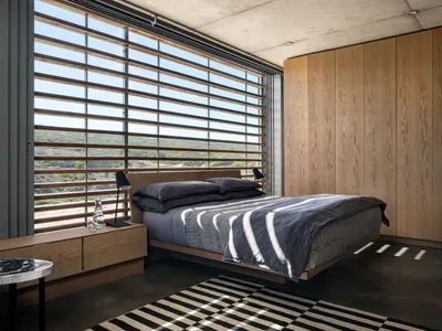 Minimalist bedroom featuring wooden furniture, concrete walls, and textiles