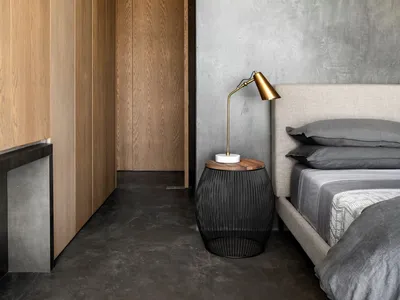 Minimalist bedroom with concrete walls, wooden furniture, and a bed with grey bedding.