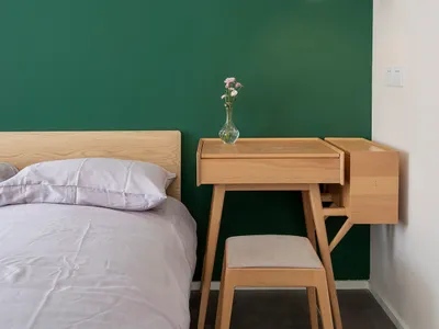Modern minimalist bedroom featuring wooden furniture, green accent wall, and pendant light above the desk.