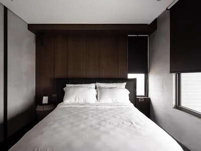 A modern minimalist bedroom with dark wood paneling and white bedding.