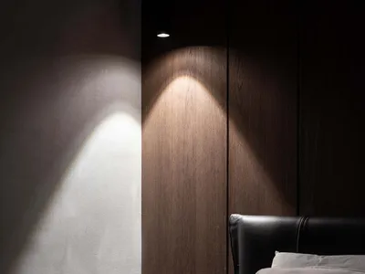 A modern minimalist bedroom featuring wooden paneling, a black headboard, and a small nightstand with a framed picture.
