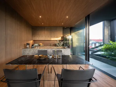 A modern residential kitchen featuring a marble countertop with stainless steel appliances and black chairs.