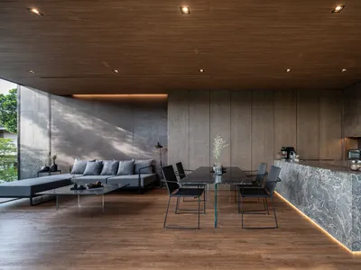 Modern living and dining area with a wooden ceiling and floor, featuring a grey sectional sofa, a black dining table with cha