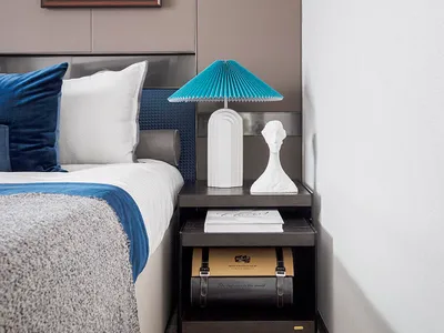 A modern bedroom featuring a double bed with blue bedding and white accents, accompanied by a black nightstand with a white l