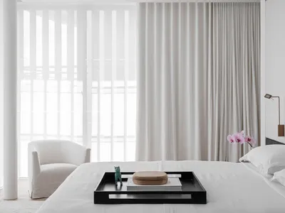 A minimalist bedroom with a white bed, white curtains, and a black tray with decorative items.