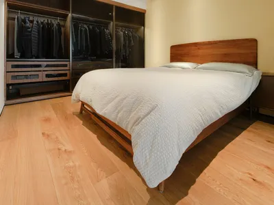 Modern minimalist bedroom featuring a wooden bed frame and a glass closet filled with clothes.