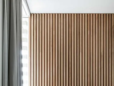 Modern minimalist bedroom featuring a grey upholstered bed with wooden slat paneling on the wall.