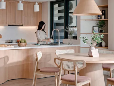 A modern kitchen with light-colored wood cabinets and a matching breakfast bar, featuring a woman washing dishes at the sink.