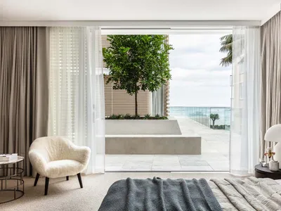 A minimalist bedroom featuring concrete walls and a large window overlooking the ocean.