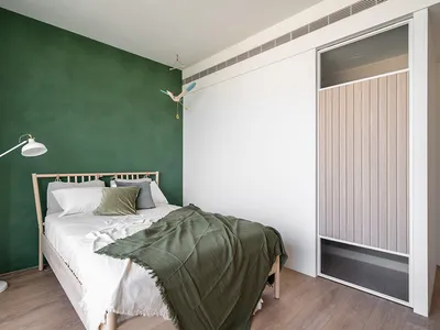 Modern, minimalist bedroom featuring a green accent wall, white bedding, and a wooden bed frame.