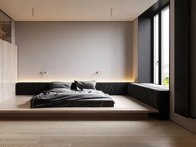 Modern minimalist bedroom featuring a platform bed with dark bedding and wooden floor, illuminated by sconces on a white wall