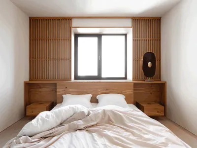 Minimalist bedroom featuring a bed with white bedding and a wooden headboard with built-in shelves.