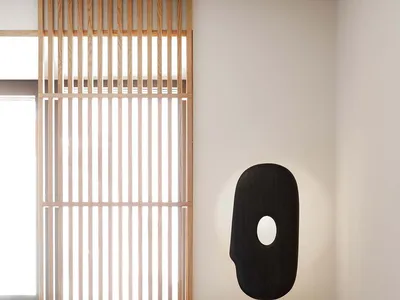 A minimalist bedroom with a wooden nightstand featuring a unique black sculptural lamp.