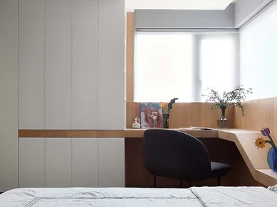 A minimalist bedroom featuring a bed, a desk with a chair, a window, and wood-paneled walls and cabinets.