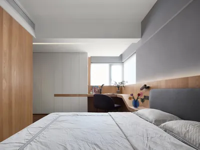 A minimalist bedroom featuring a wooden headboard and a window allowing natural light to illuminate the space.