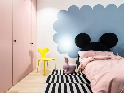 Minimalist bedroom featuring a pink bed with black Mickey Mouse ears headboard, a yellow chair, and a black and white striped