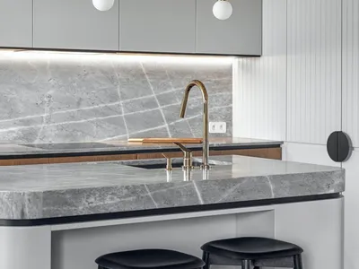 A modern kitchen with a marble countertop, featuring a bar with stools and a sleek faucet with a brass finish.