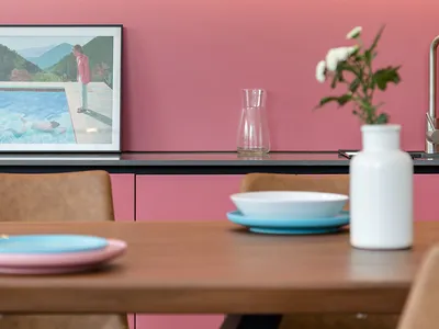 Modern kitchen featuring pink cabinets and wooden furniture, with plates and a vase.