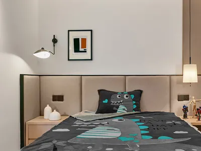 A modern bedroom with a brown padded headboard, a dinosaur-patterned blanket, and a framed abstract painting on the wall.
