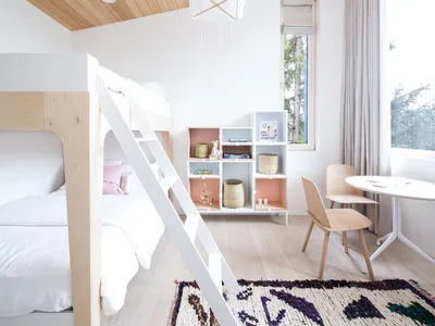 A minimalistic bedroom featuring a wooden bunk bed with a white ladder, a wooden chair, and a wooden bookshelf.